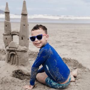 Thalisson sits on the beach next to his sandcastle