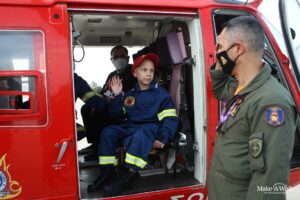 A young boy wearing a fireman costume giving a high-5 to a firefighter from a red helicopter