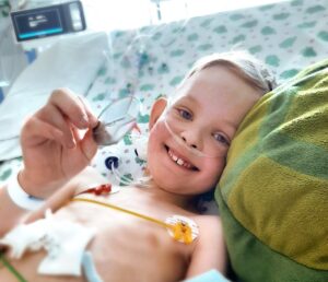 A smiling child wearing electrograms in a hospital bed