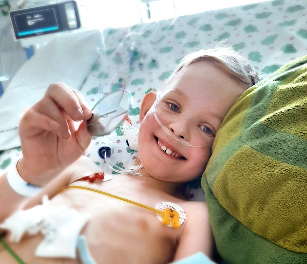 A smiling child wearing electrograms in a hospital bed