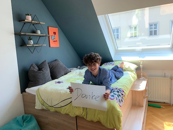 A young boy lying on a bed holding a thank you message