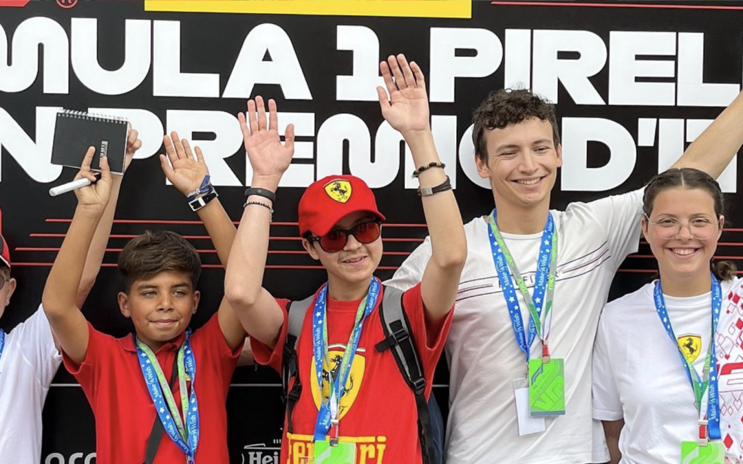 A group of wish children at a Formula 1 event raise their hands in celebration