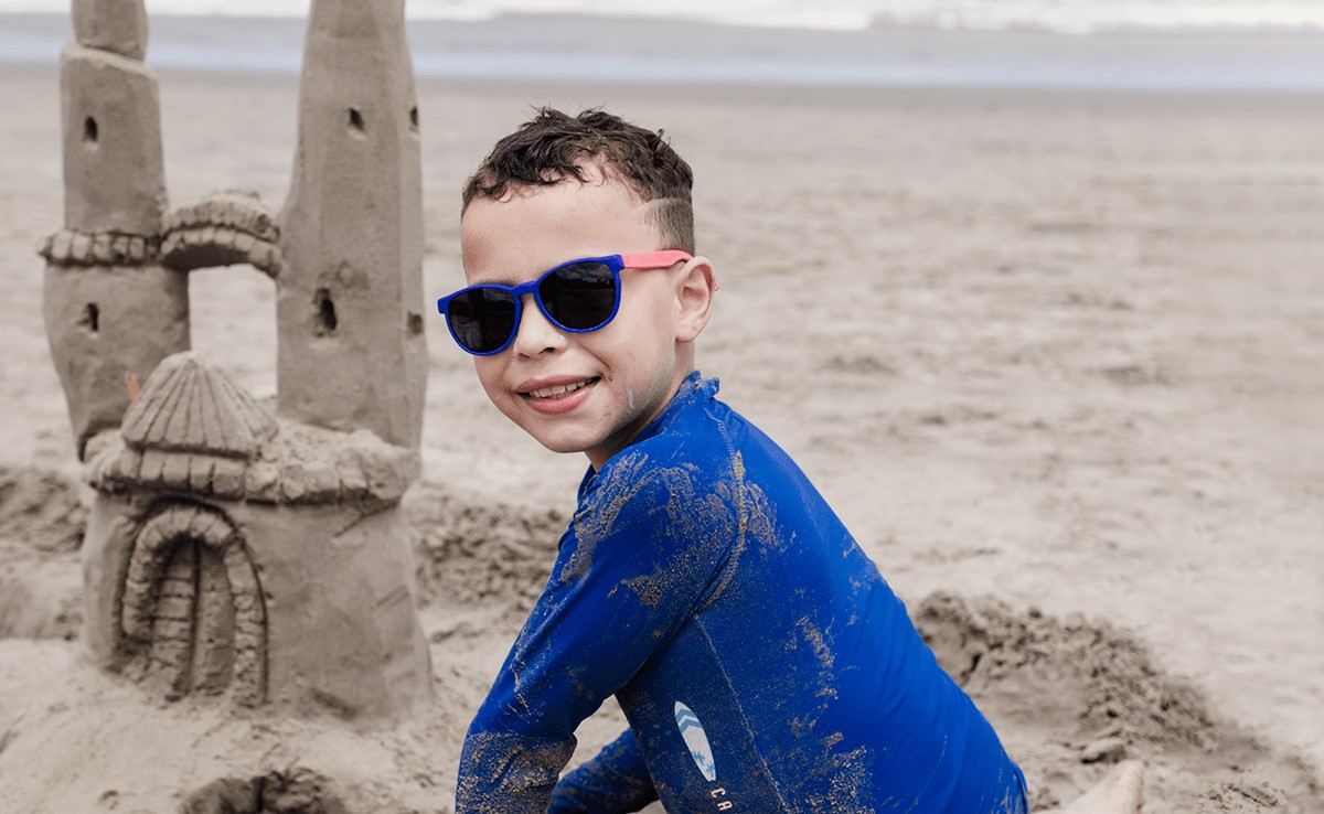 a young boy posing in front of a sandcastle on the beach