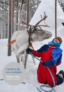 Boy wearing snow suit in snow with reindeer