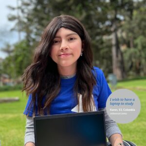 Girl sitting on the grass holding a laptop, wearing a Make-A-Wish t-shirt