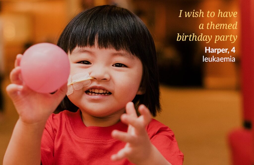 A young child with a nasal tube smiles and holds a pink balloon. She wears a red shirt. Text reads: I wish to have a themed birthday party. Harper, 4, leukaemia.