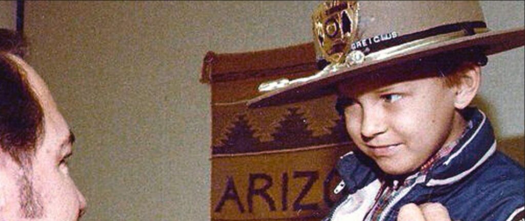 A young boy wearing a large police officer’s hat smiles while looking at an adult. A woven wall hanging behind them partially reads “ARIZ.”—capturing the joy Make-A-Wish brings to families through our policies and support.