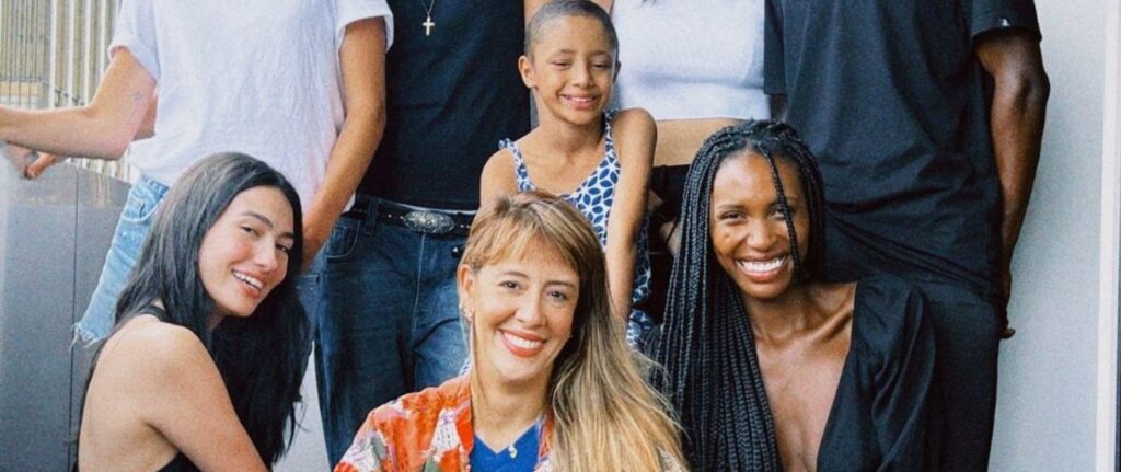 A group of seven people, including adults and a child, pose closely together and smile at the camera. Their happiness shines through, much like the joy brought by Make-A-Wish, as they relax in casual summer clothing outdoors.
