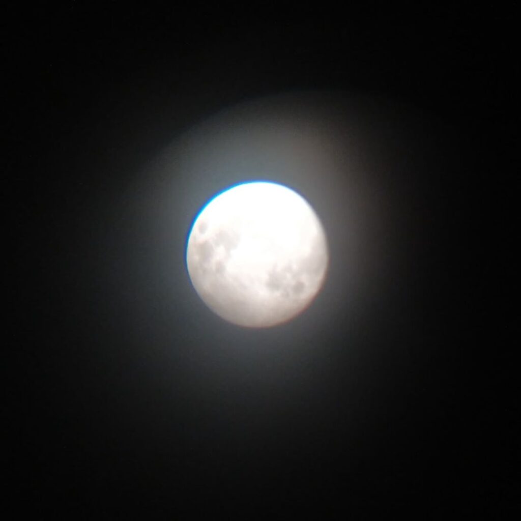 A bright, glowing full moon is surrounded by a soft halo against a dark night sky. Some surface details and craters are visible on the moon, making Vendants wish to have a telescope feel even more magical.