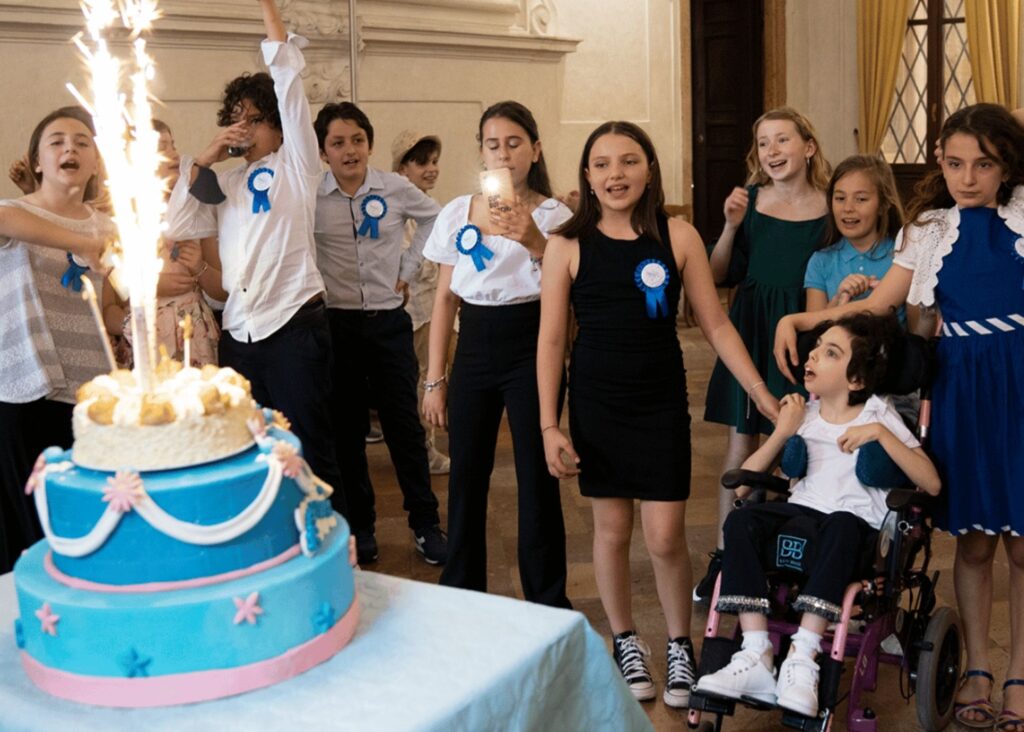 A group of children, some wearing blue ribbons, excitedly watch a large blue and pink cake with sparklers. The scene is festive and joyful as Sofias wish to dance with Prince Charming adds a touch of magic to the celebration.