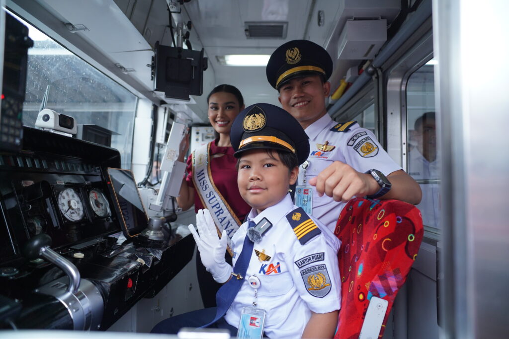 A smiling woman in a sash sits inside a train cab with two conductors, one adult and one child, all posing cheerfully for the camera—capturing the joy of Ying Xuan's wish to be a mermaid in an unexpected setting.