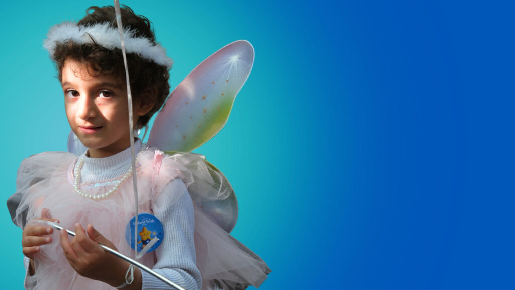 A young child wearing a white halo headband, fairy wings, a pink and white dress, and a beaded necklace holds a silver wand. The background is a smooth blue gradient.