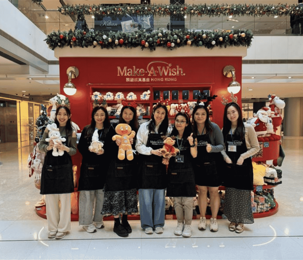 Seven women smile in front of a festive Make-A-Wish Hong Kong display during a Robert Half fundraising event, holding soft toys among holiday decorations and stuffed animals on the vibrant red backdrop.