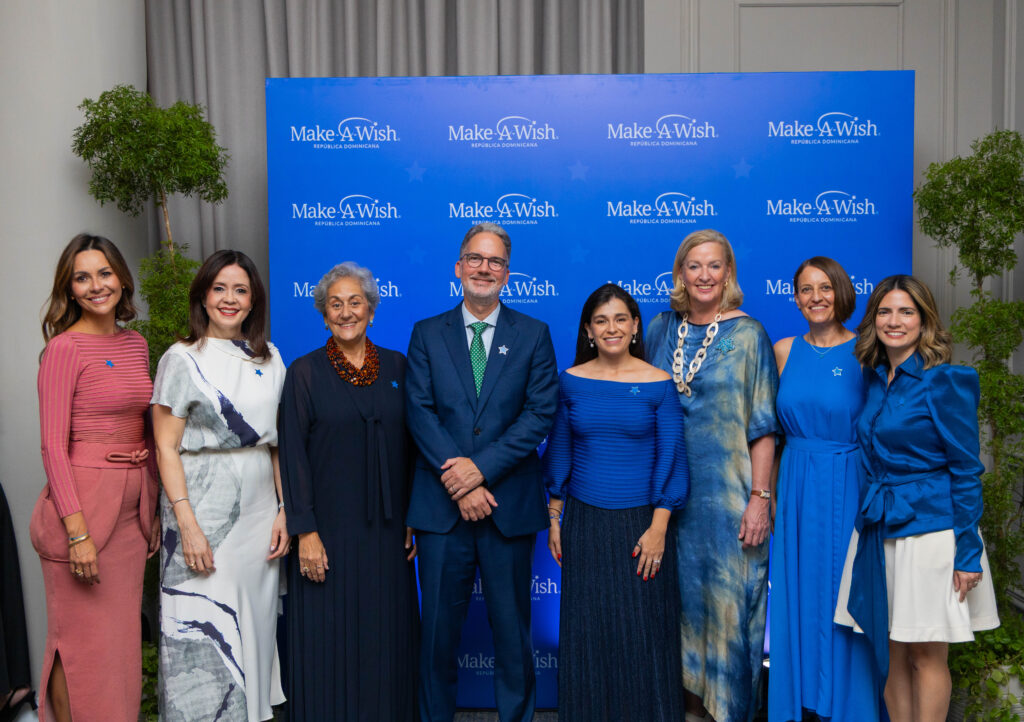 Eight people stand in a row in front of a blue Make-A-Wish República Dominicana step-and-repeat banner as the organisation launches in the Dominican Republic.