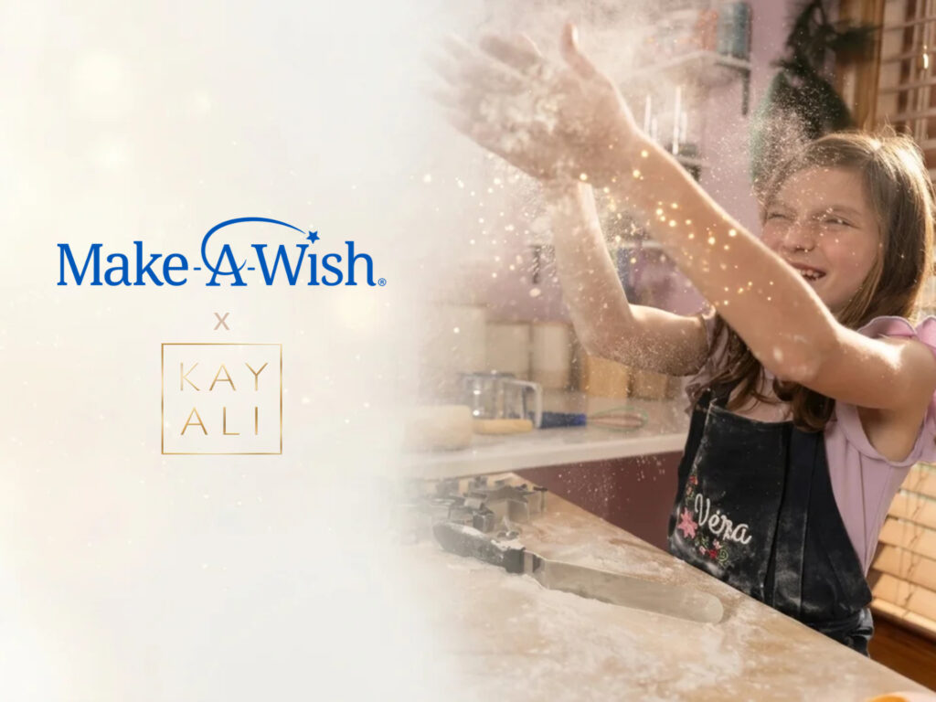 A child in a K apron claps hands together, creating a cloud of flour, with the Make-A-Wish and KAYALI logos overlaid on the left.